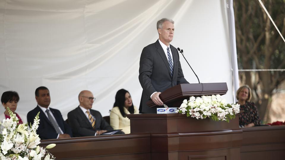A man wearing a suit and tie speaking from a pulpit outside.