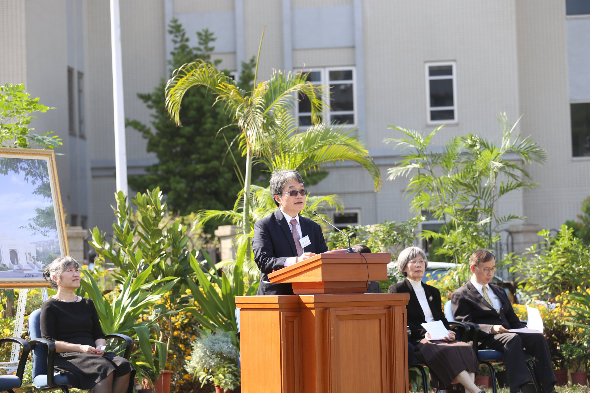 A man wearing a suit and tie and speaking from a pulpit outside.