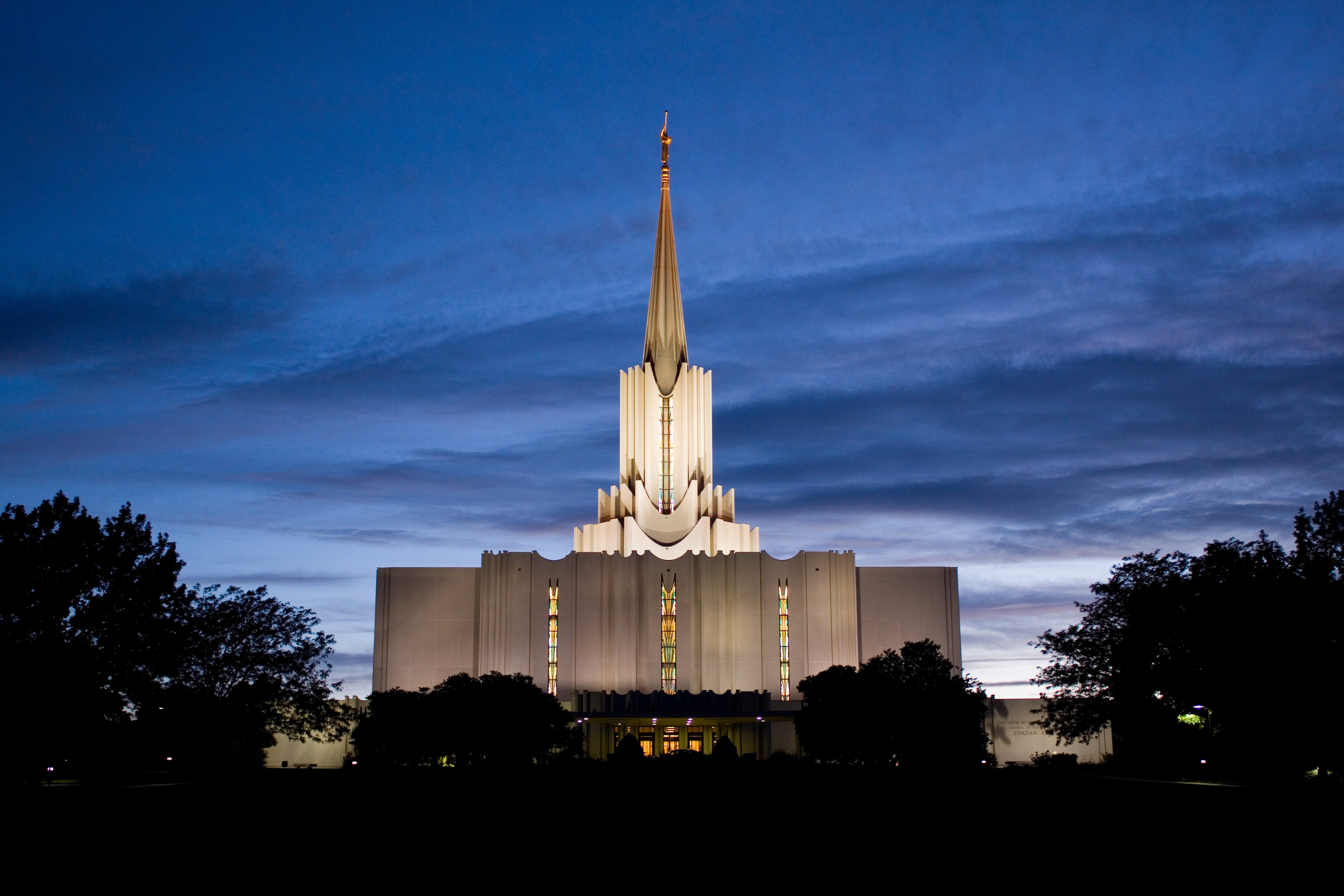 A nighttime view of the Jordan River temple, a white building with cast stone and white marble chips on the exterior.  