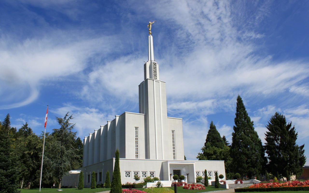 The Bern Switzerland Temple, a white building with a spire topped by a golden statue of an angel blowing a horn.