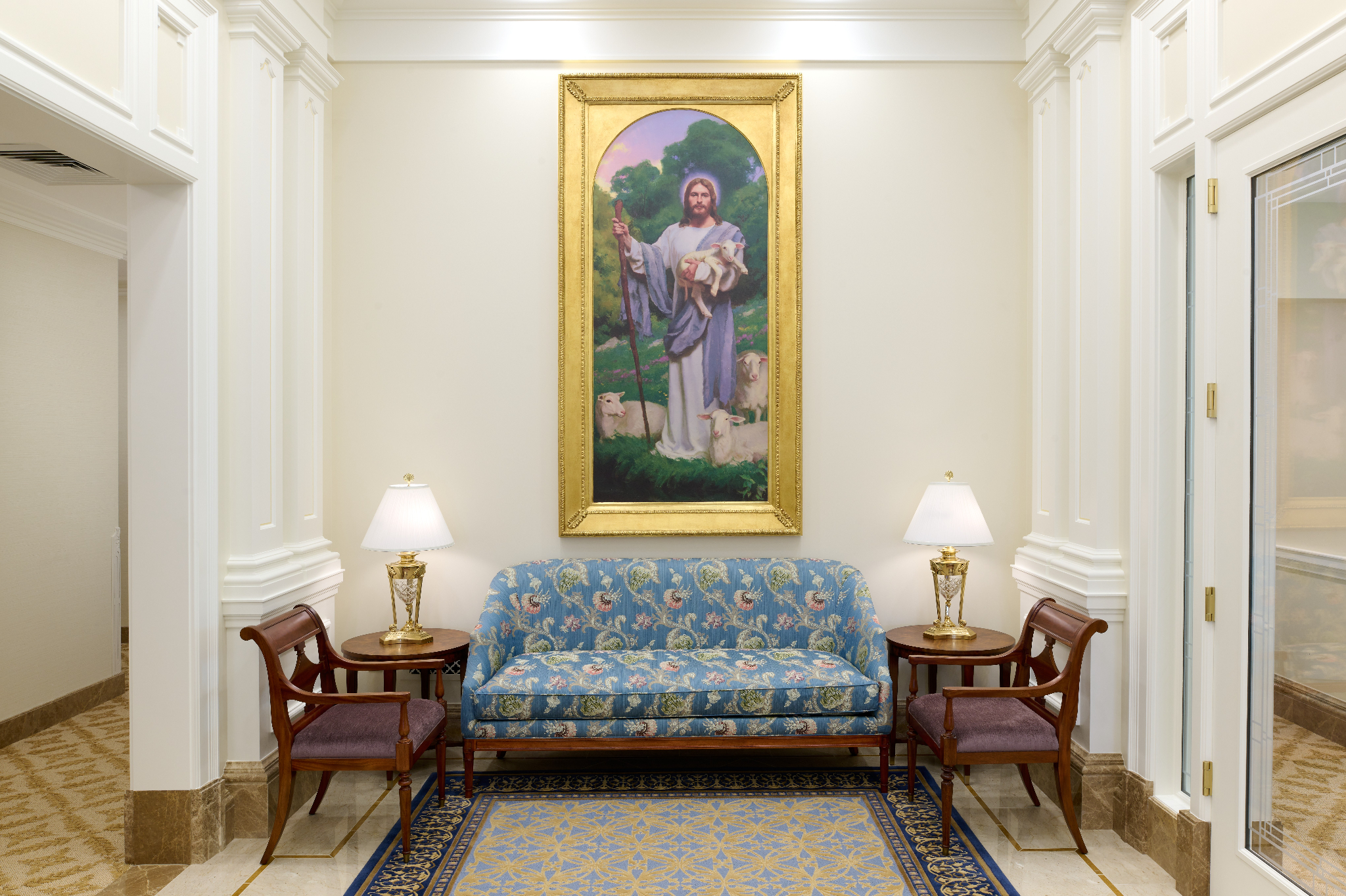 A white room with a light-blue couch under a painting of Jesus Christ holding a sheep.