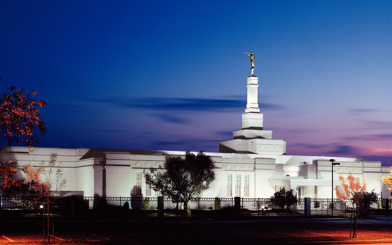The exterior of the Fresno temple, a gray one-story building with a multilevel tower and spire on top, at sunset.