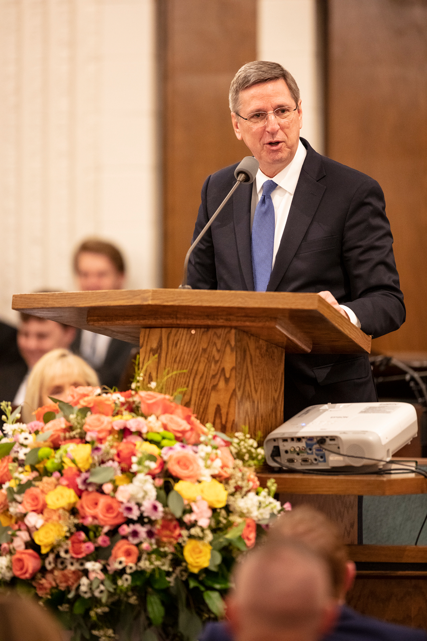 A man wearing a suit and tie and speaking from a pulpit inside.