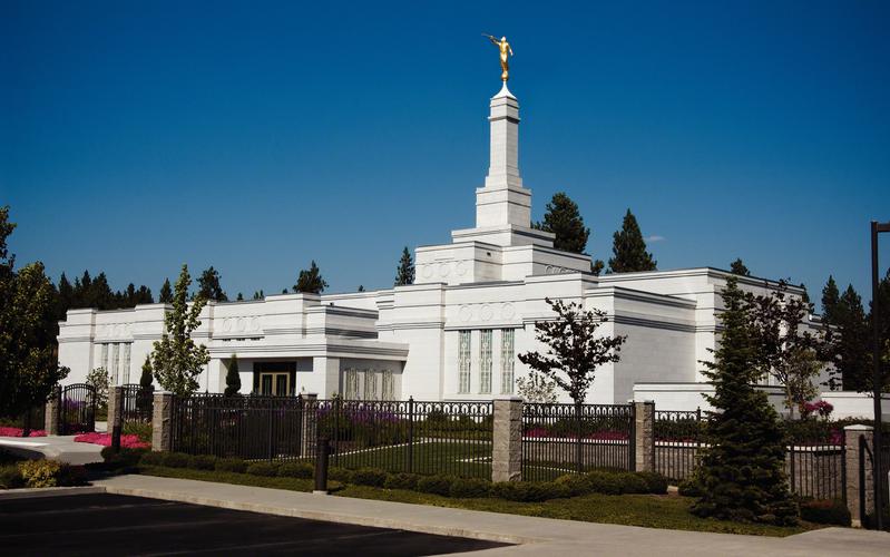White Spokane Washington temple surrounded by trees and a fence. 