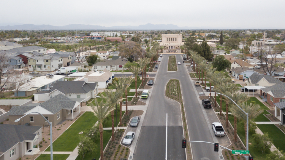 An aerial view of a wide road with houses around it and the Mesa temple in the distance.