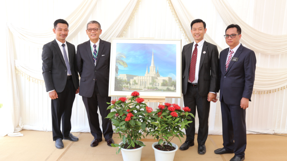 Four men in suits and ties standing around a rendering of the Phnom Penh Cambodia Temple and smiling at the camera.