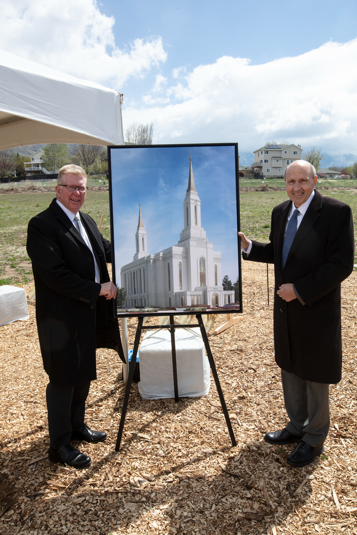 Two men in suits and ties standing next to a picture frame with a picture of the Lindon temple rendering inside.