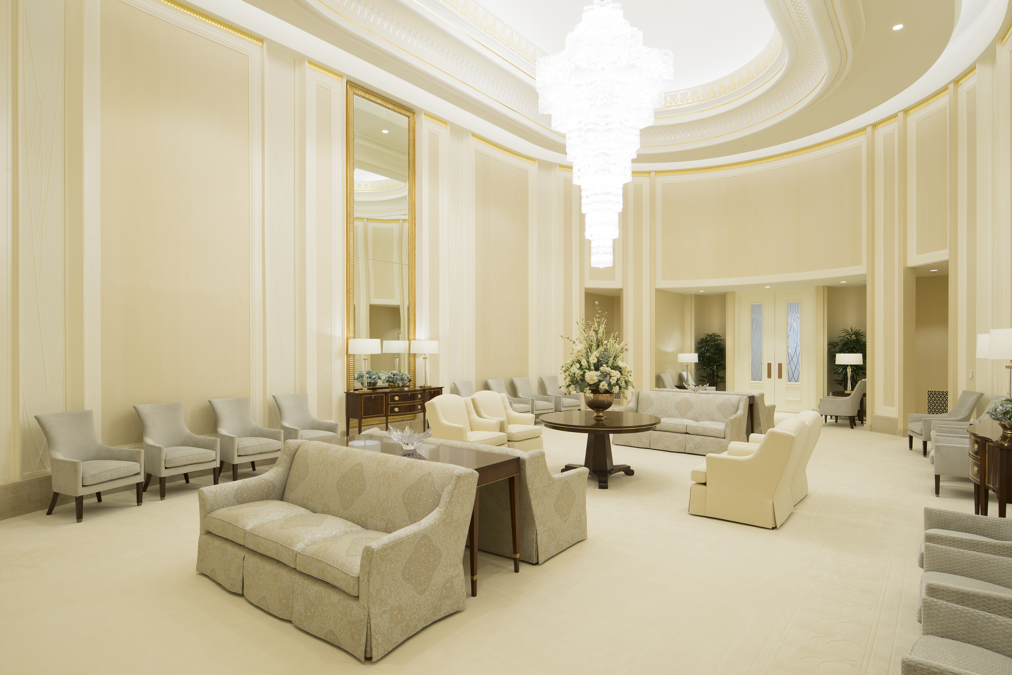 A white room with white and gray furniture around, with a large, clear-glass chandelier hanging from the middle of the ceiling.
