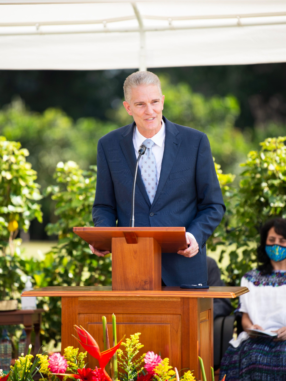A man in a suit and tie speaking from a pulpit outside.