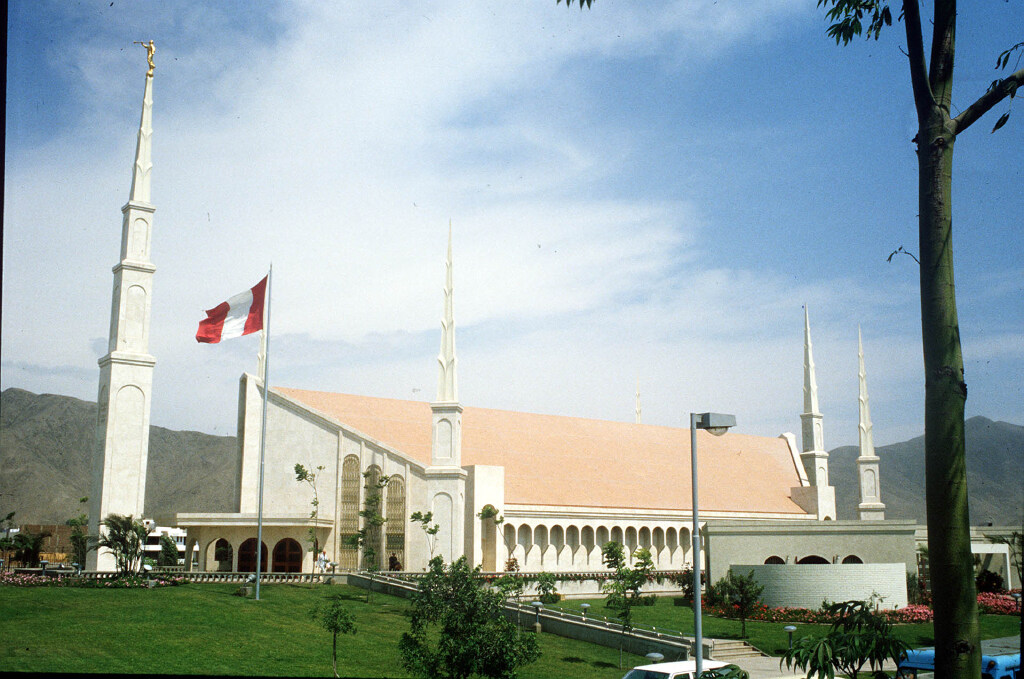A side view of the Lima Peru Temple, a building with a red peaked roof on top.
