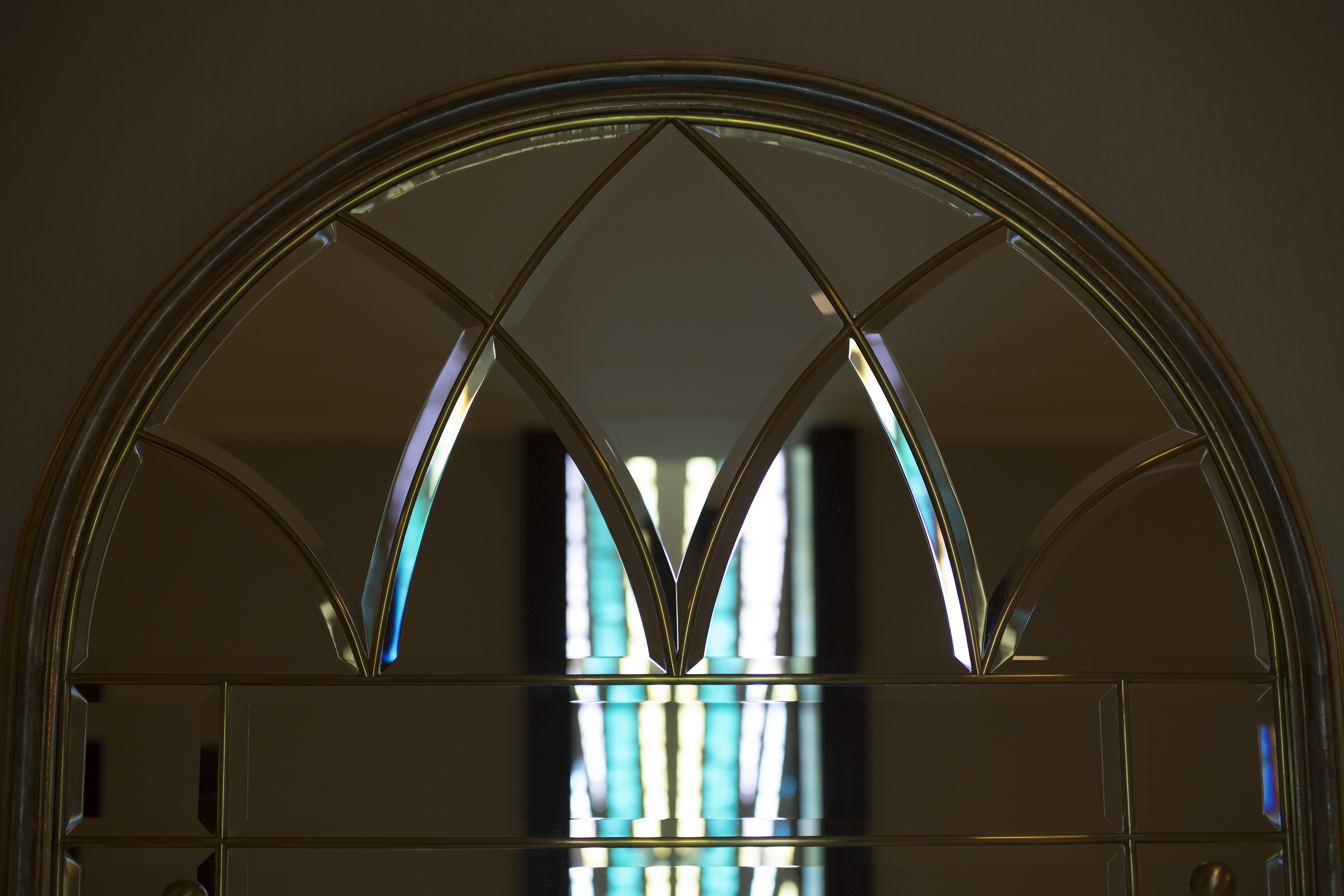 A close-up of an arched mirror reflecting white and light blue from an art glass window.