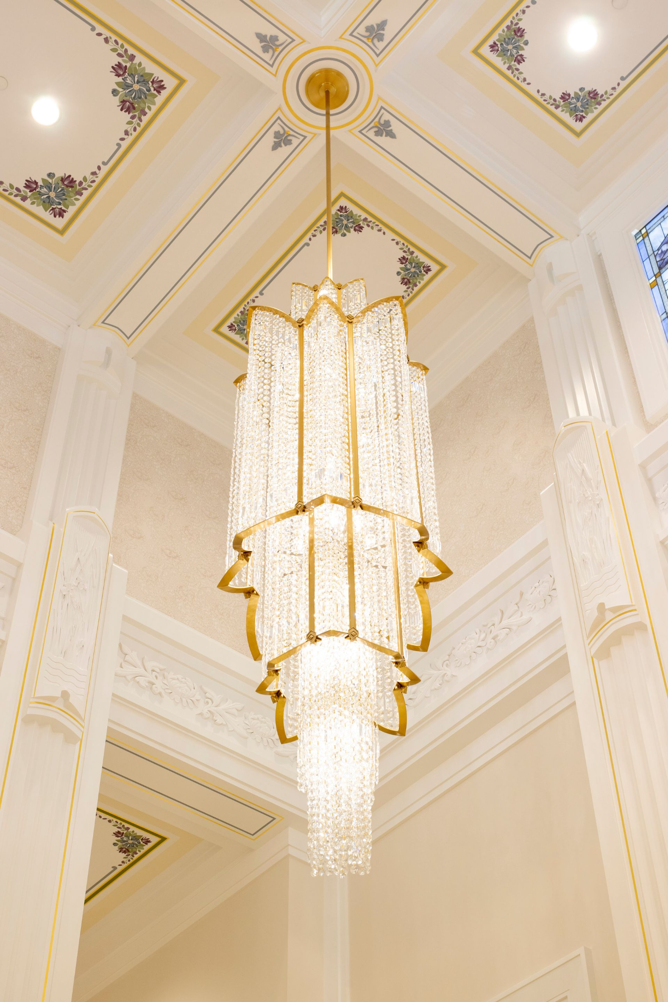 A tall white chandelier hanging from a white ceiling.