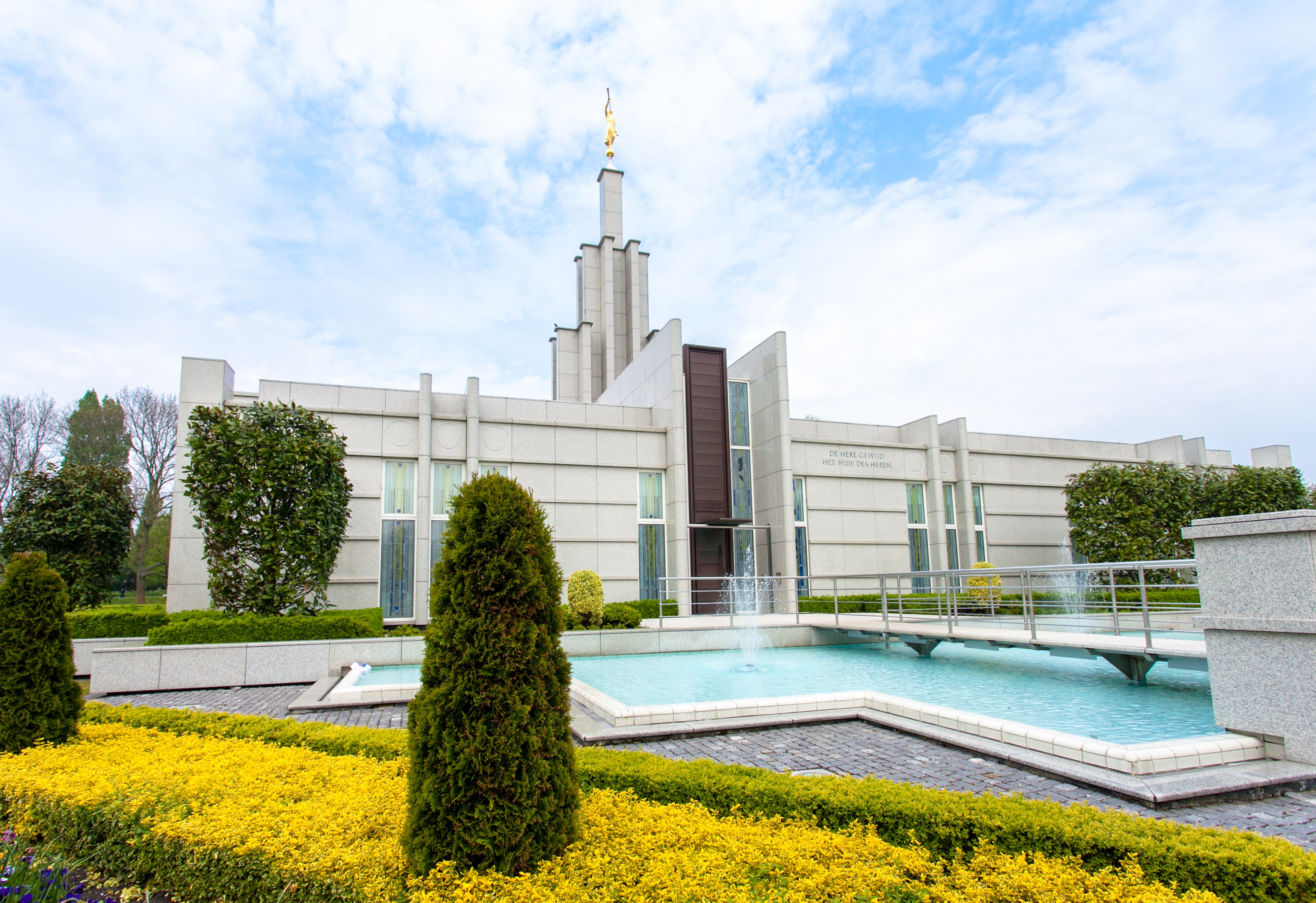 The Hague Netherlands Temple, a white building with a spire topped by a golden statue of an angel blowing a trumpet.