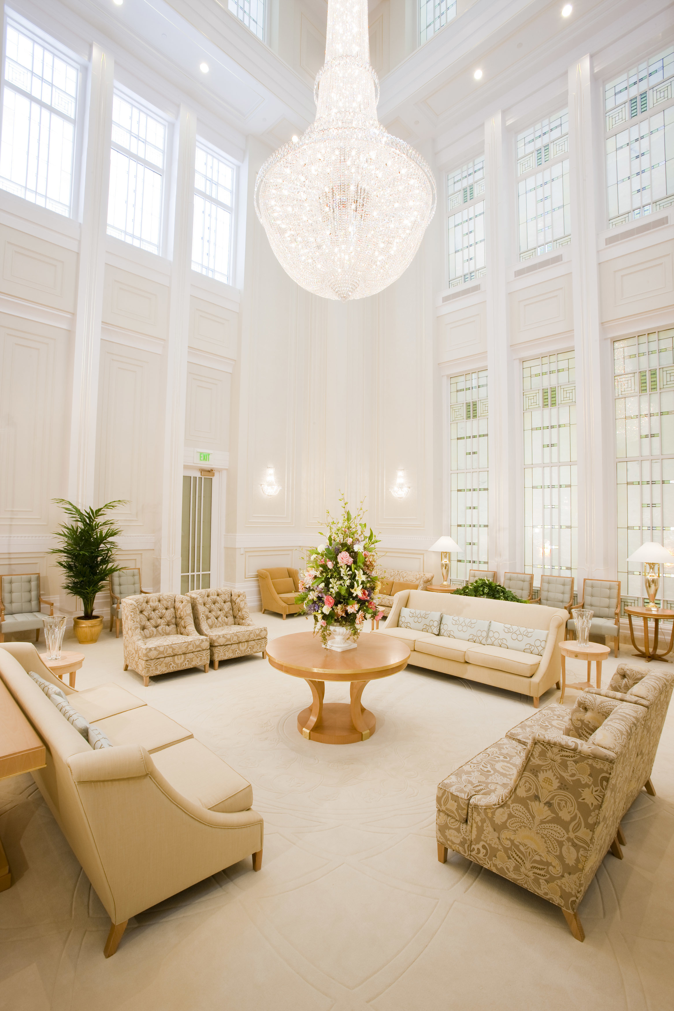 A tall, white room with white couches and a tall chandelier hanging from the ceiling.