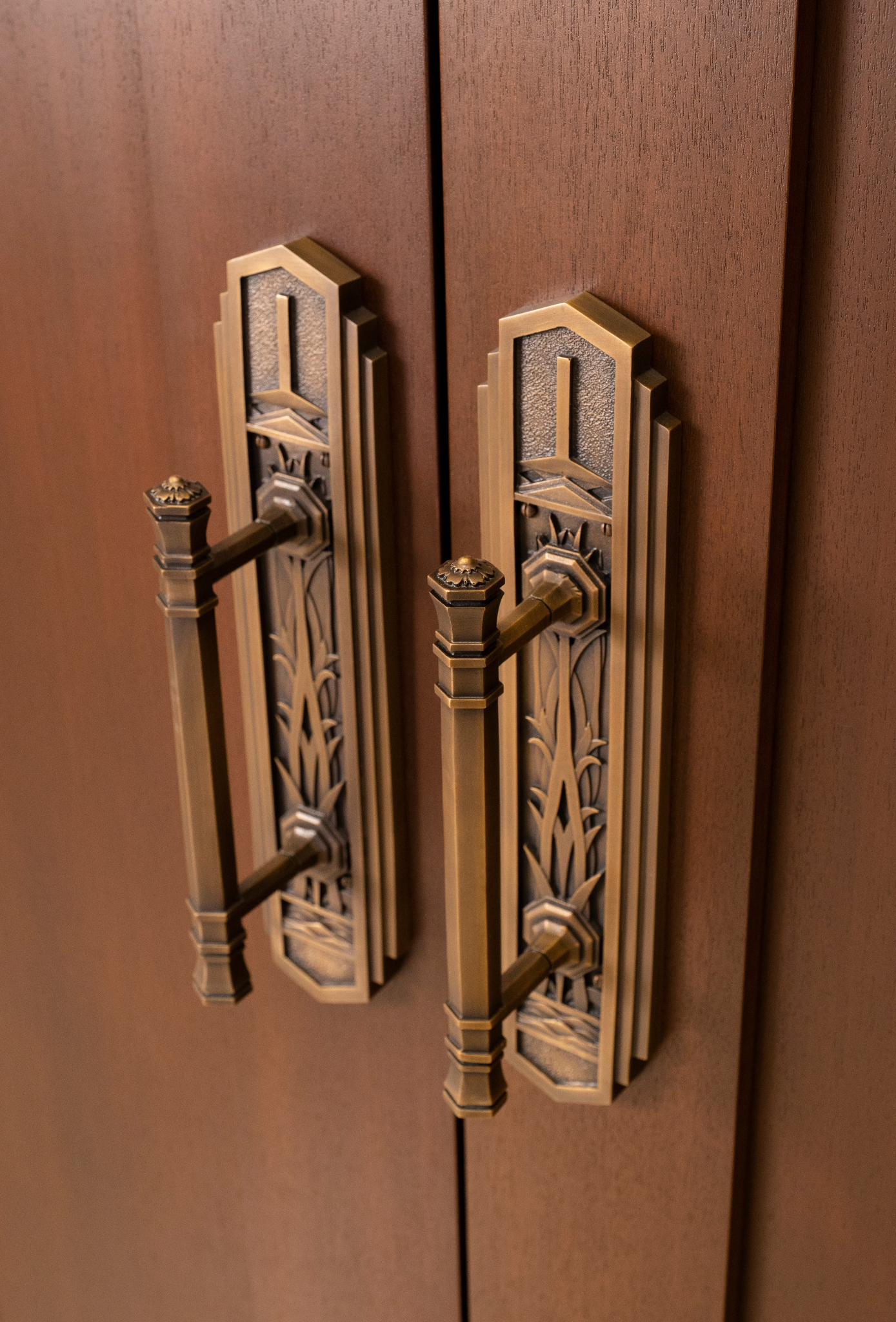 A close-up of metal door handles carved with the designs of water and wetland grass.
