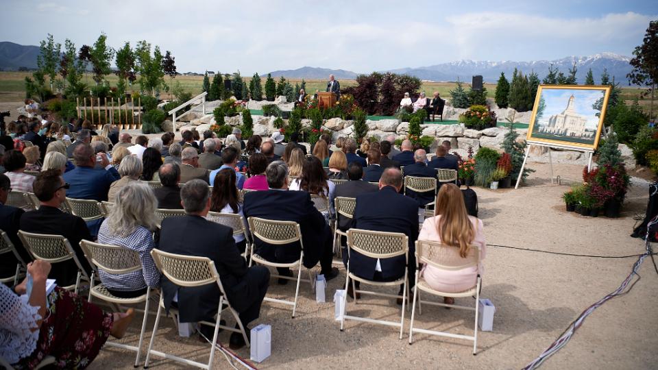A large group of people sitting in chairs outside and listening to a speaker at a pulpit.