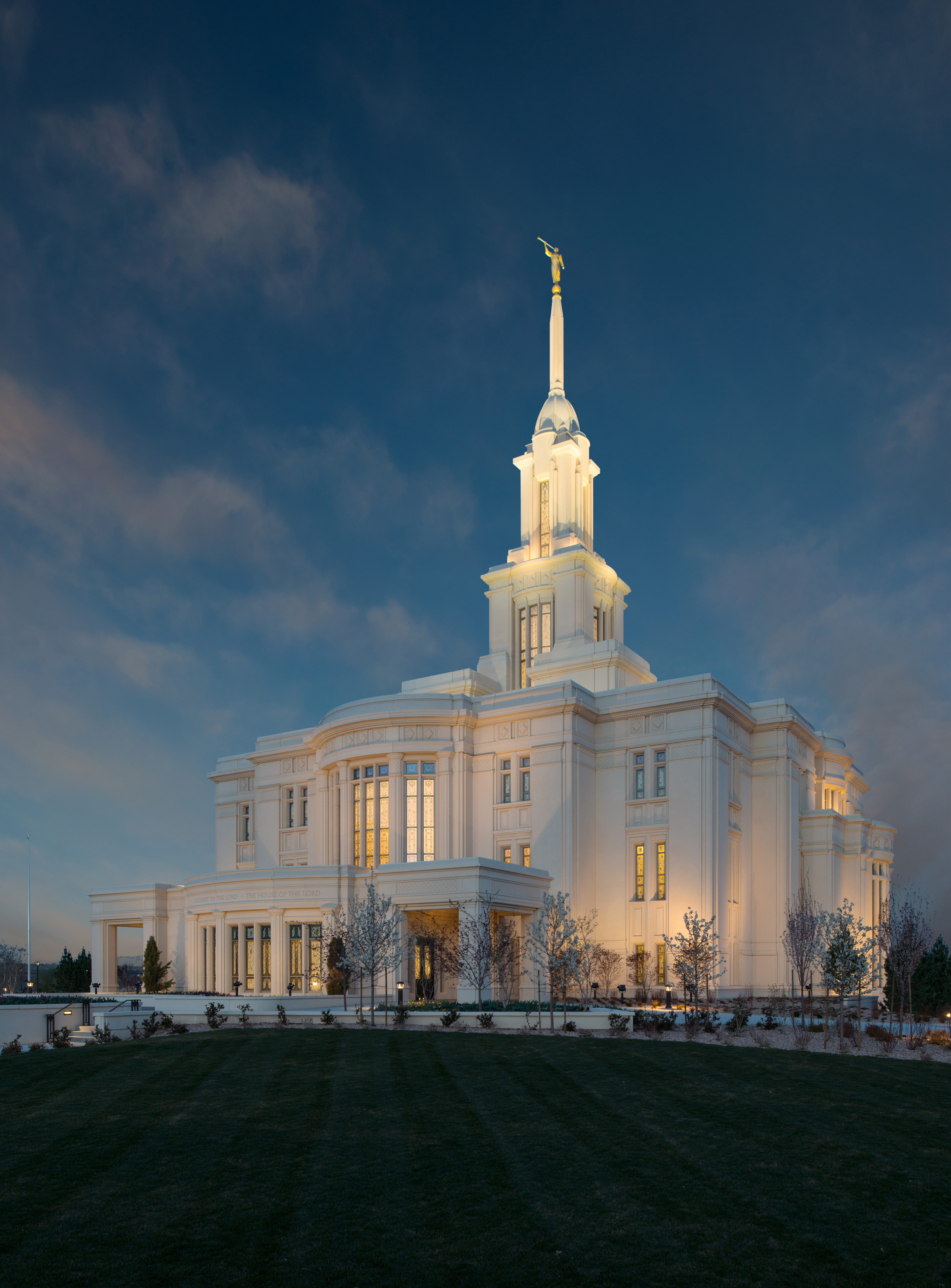 The Payson Utah Temple, a white building with a steeple, lit by external lights.