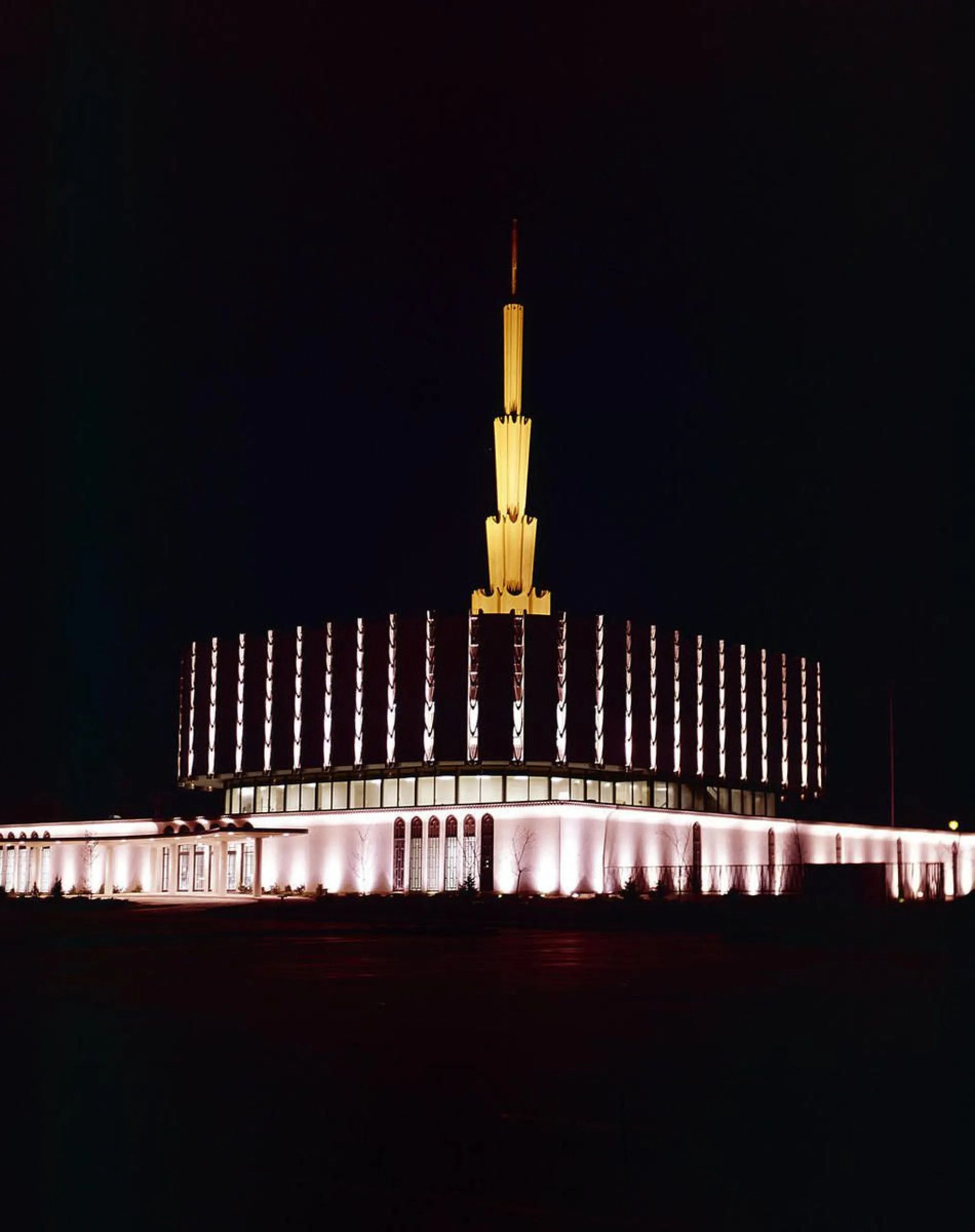 A nighttime view of the original Ogden Utah Temple, dedicated in 1972, that had a flat, round base with a spire in the center.