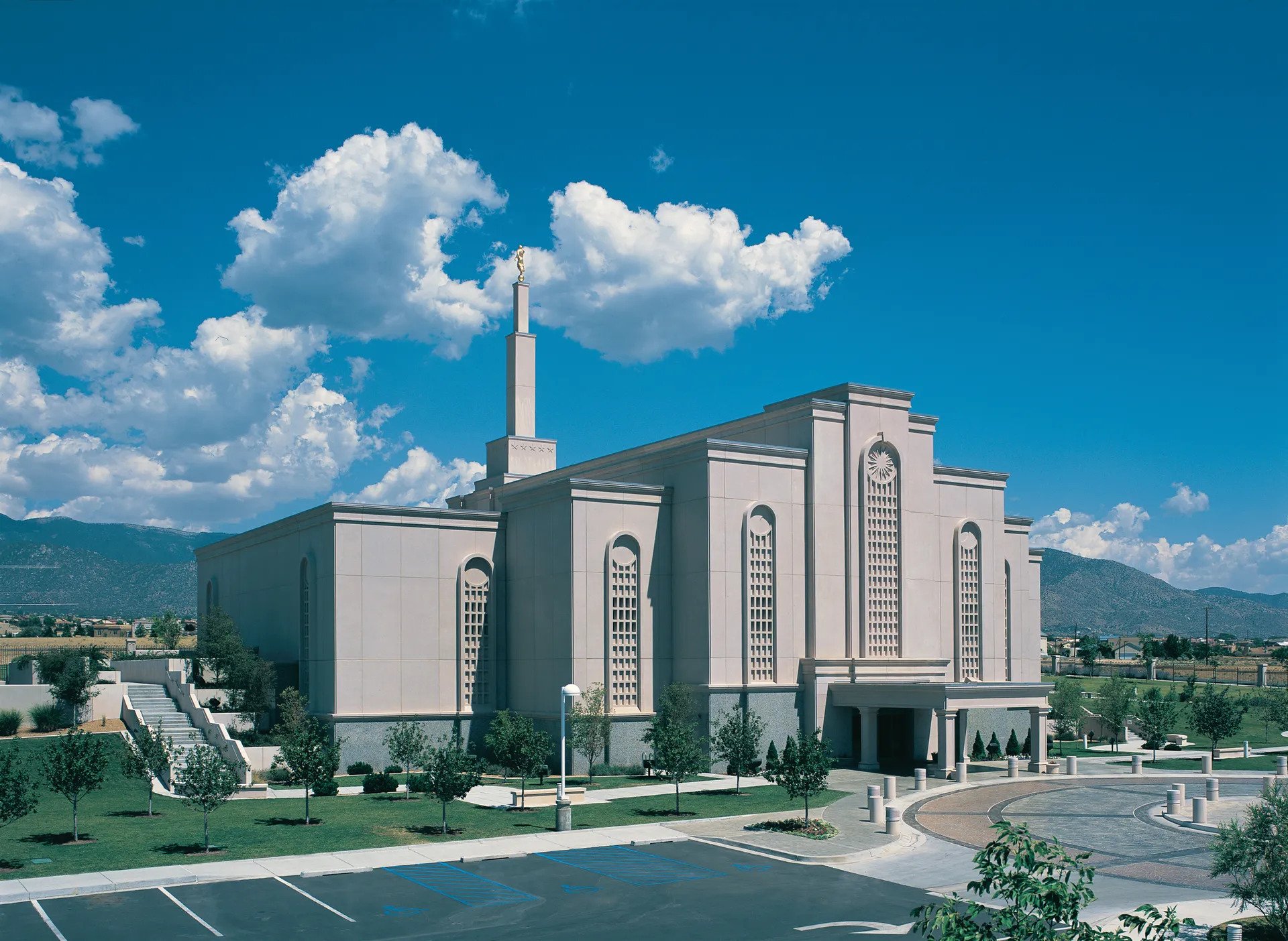 The exterior of the Albuquerque New Mexico Temple, a white building with flat roofs cascading down from a center spire.
