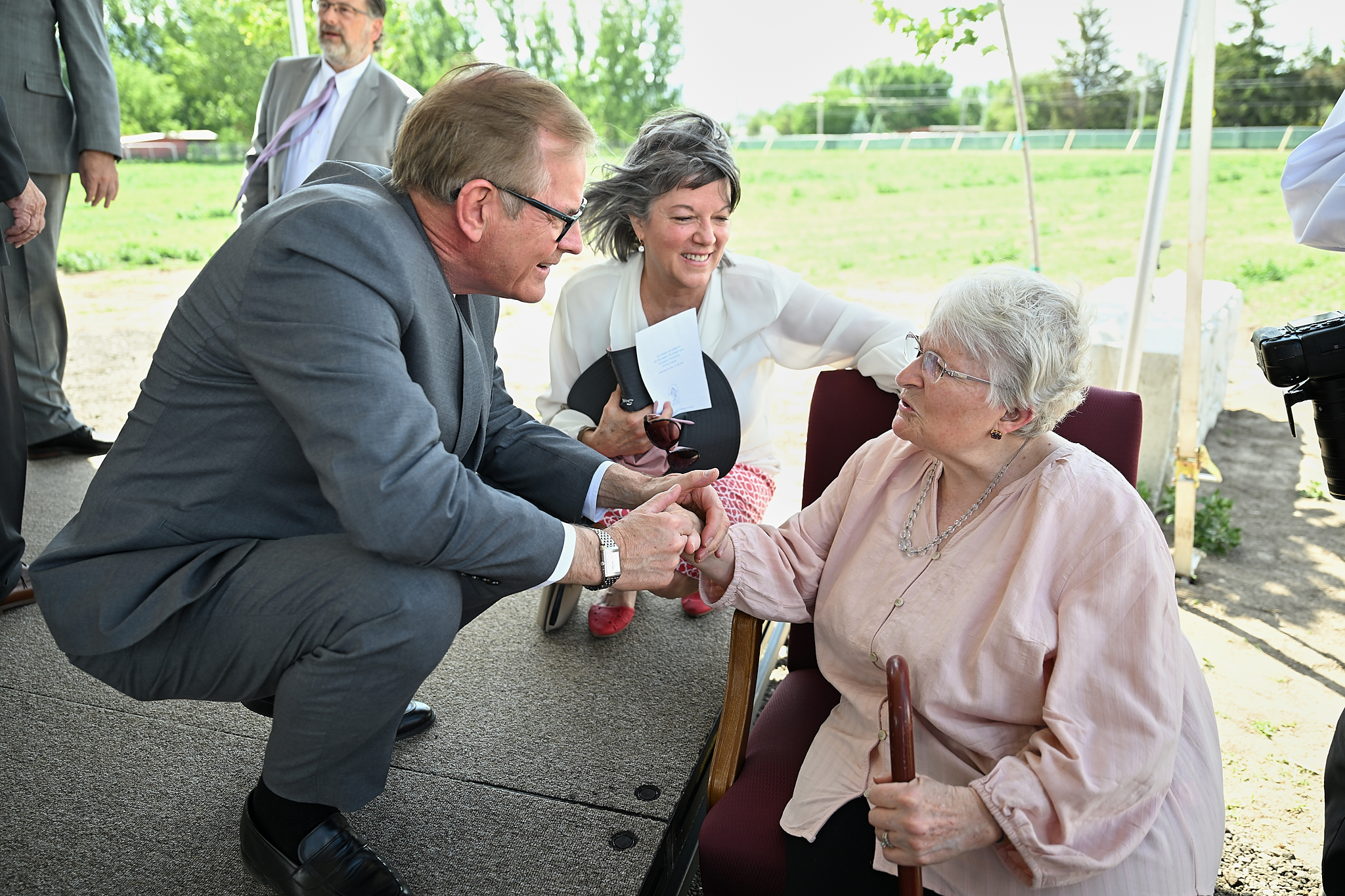 Elder Stevenson wearing a suit and shaking the hand of a woman in a pink dress sitting down.
