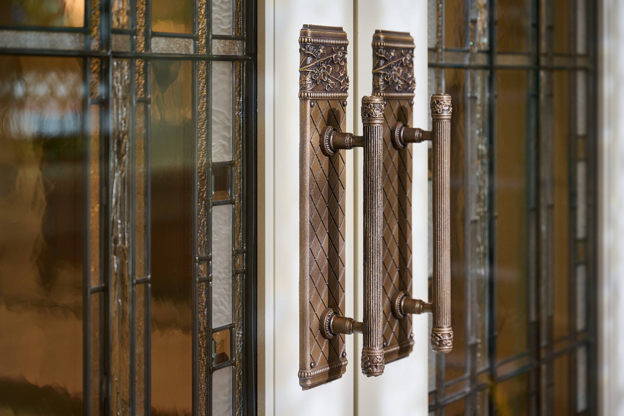 A close-up of metal door handles on doors with stained glass across it.