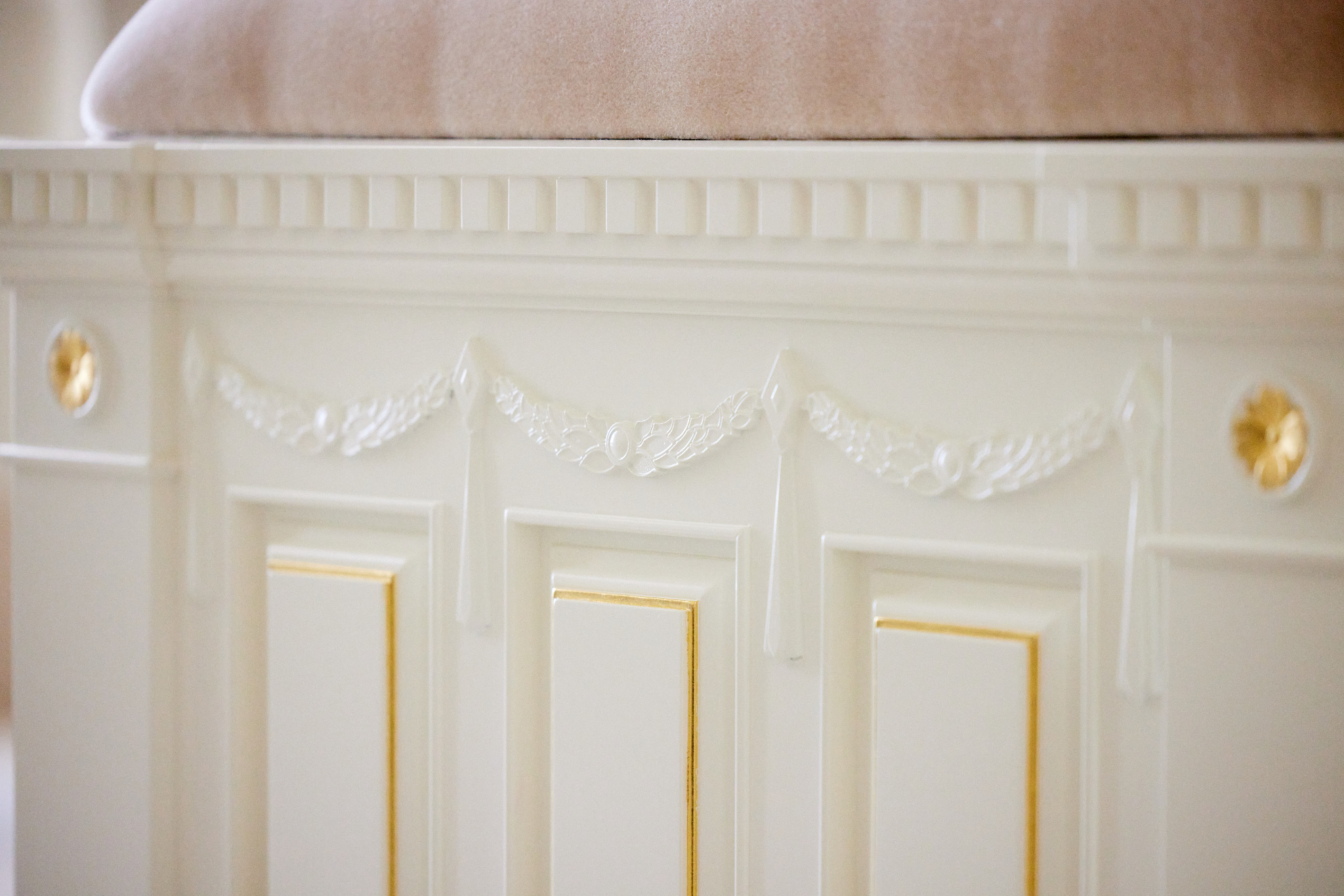 A close-up of wooden millwork painted white with tiny gold lines.