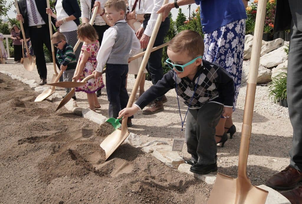 A row of people holding shovels and digging into the ground, including three Primary children.