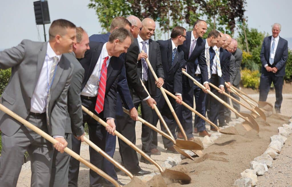 A row of men in suits and ties holding shovels and digging into the ground.