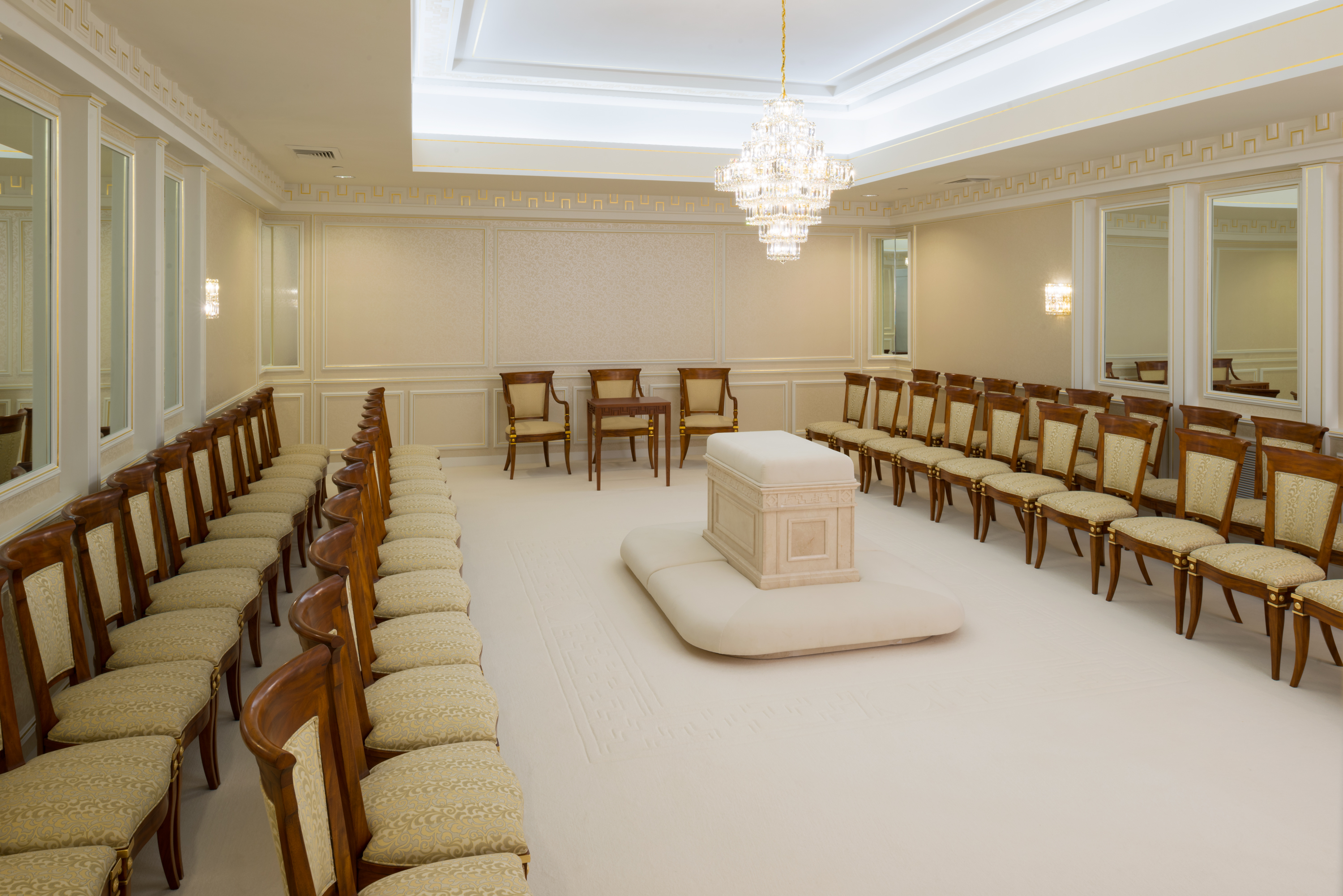 Two rows of chairs on both sides of the room facing a white altar in the center, with mirrors on two opposite walls.