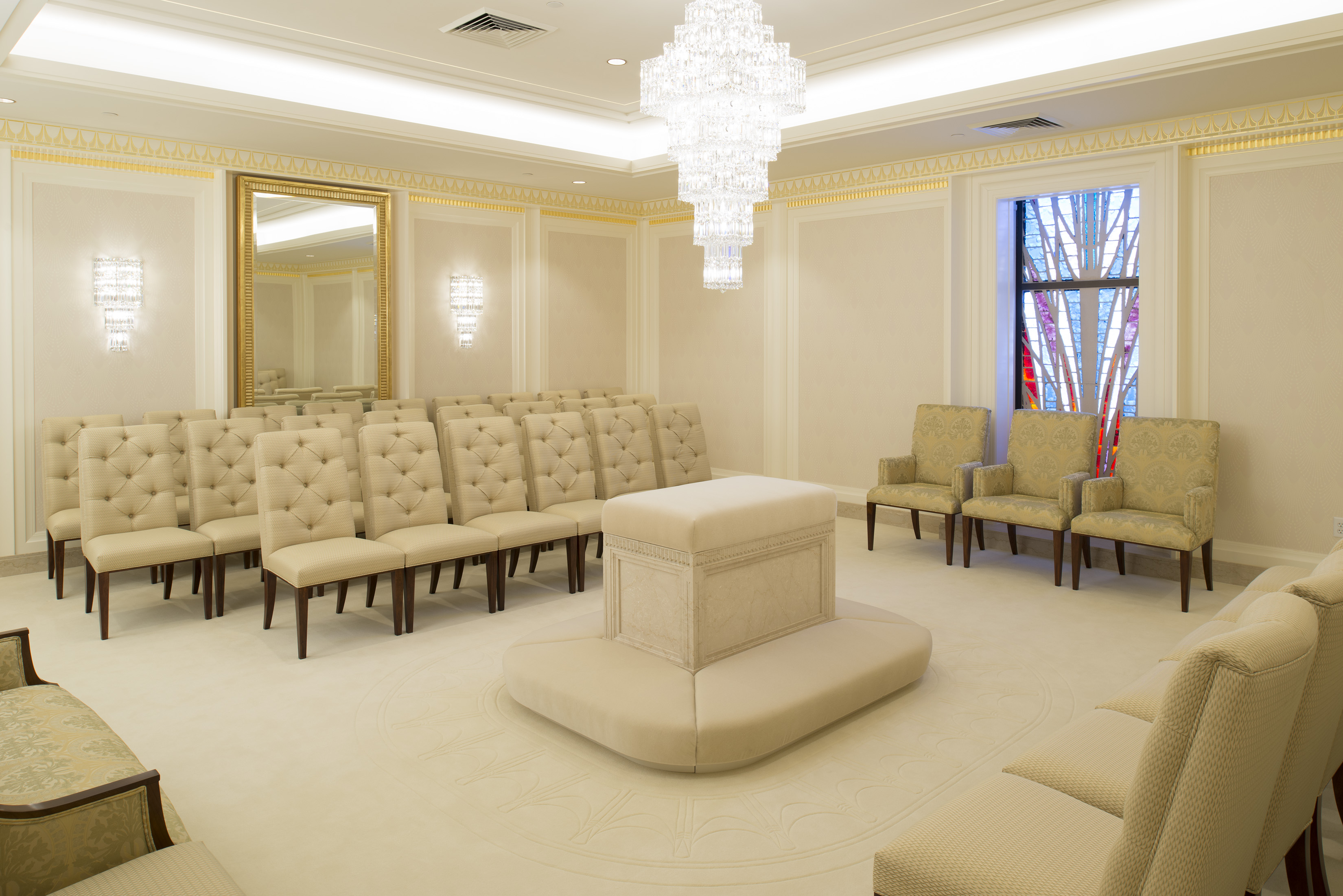 A white room with white chairs lined around the room and a white altar in the center of the room.