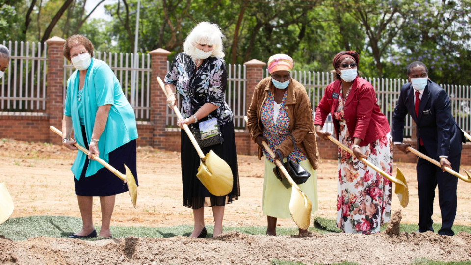 A row of people in Sunday best holding ceremonial golden shovels and digging into the dirt.