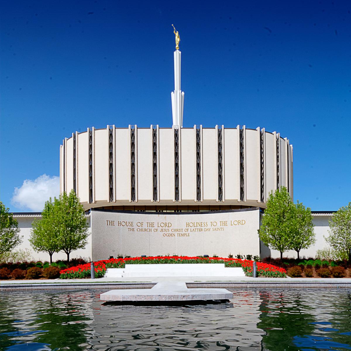 The exterior of the original Ogden Utah Temple, dedicated in 1972, that had a flat, round base with a spire in the center, with a reflecting pool in front of the building.