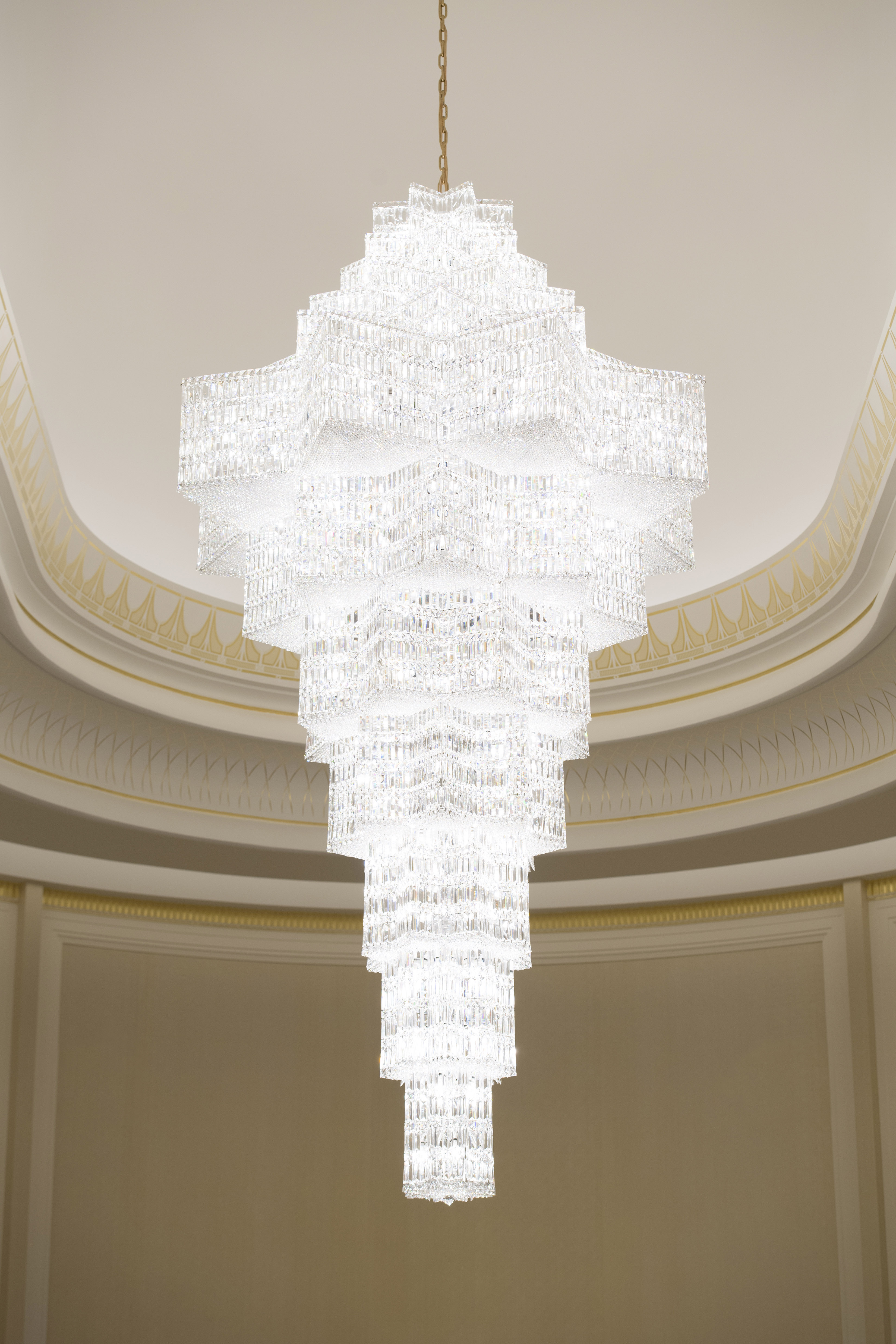 A close-up on an illuminated chandelier, a large tower of glass hanging from the ceiling.