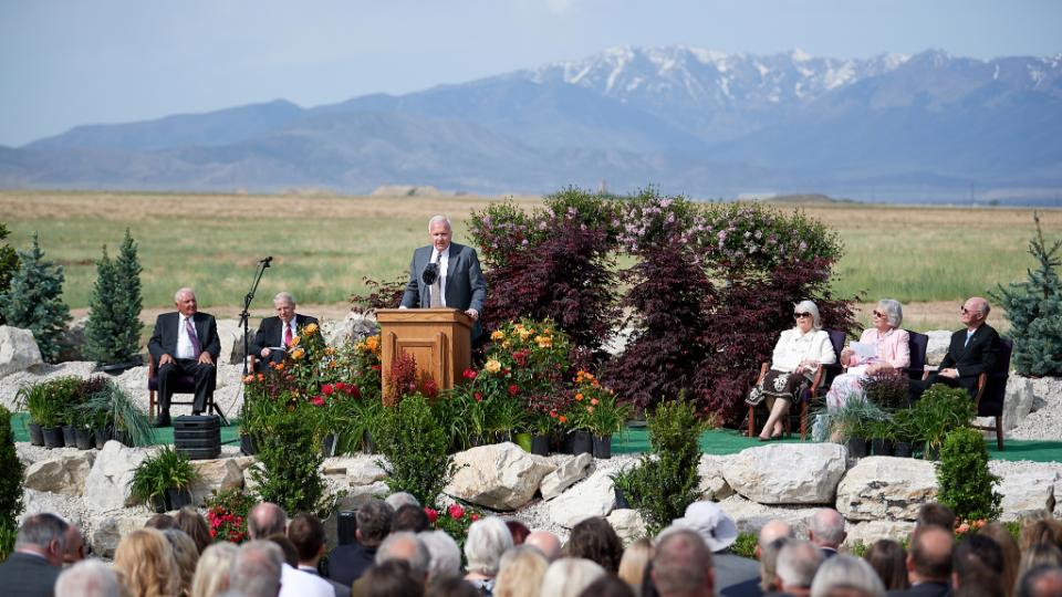 A man wearing a suit and tie and speaking to a congregation from a pulpit outside.