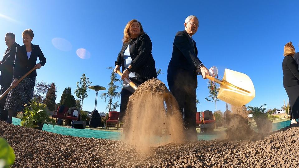 A low angle of people holding ceremonial golden shovels and scooping a shovelful of dirt from the ground.