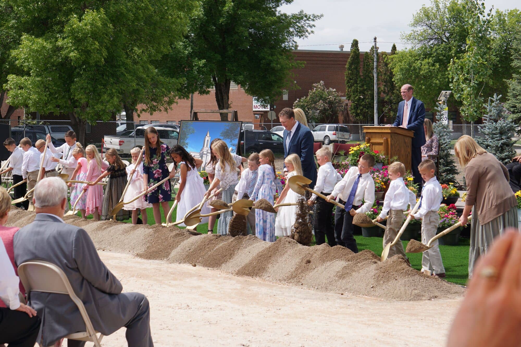 A row of Primary-aged boys and girls in Sunday best holding ceremonial golden shovels with a scoop of dirt.