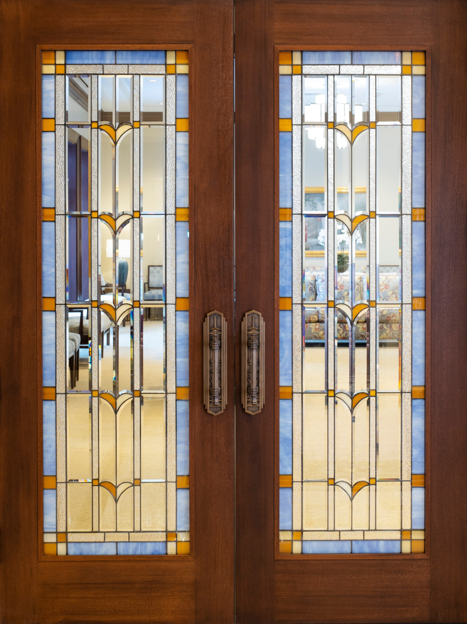 A close-up of two wooden doors with blue, orange and clear art glass in the middle.