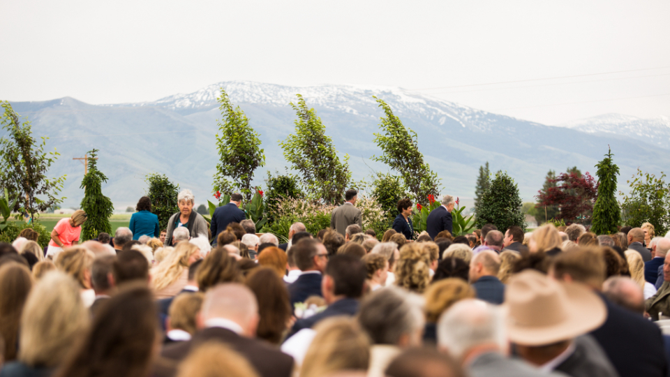 Guests wait for the Burley Idaho Temple groundbreaking ceremony to begin. There are mountains in the background.
