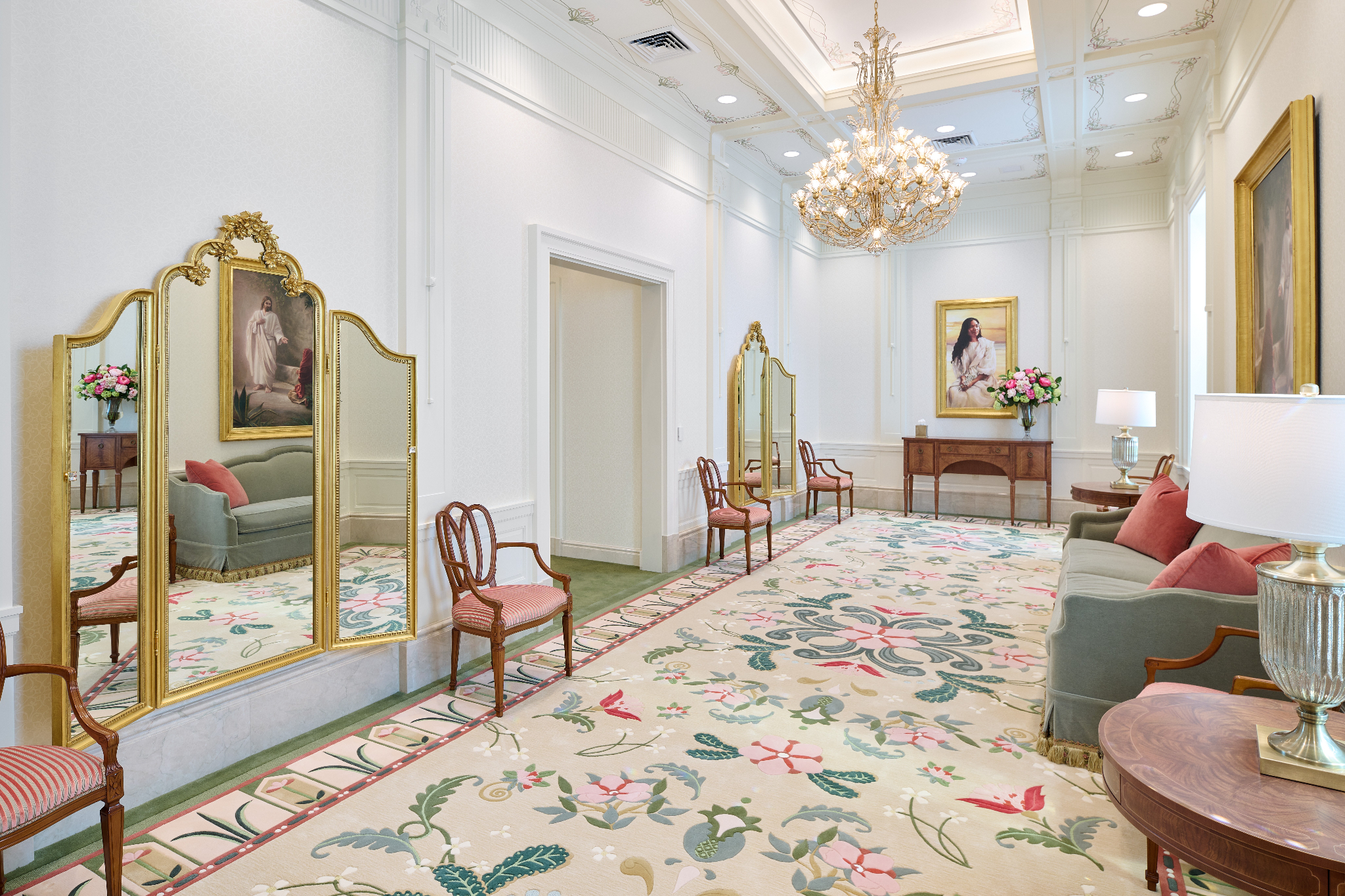 A white room with a large floral-patterned rug on the floor, with two mirrors having a gold frame and hanging from the wall.
