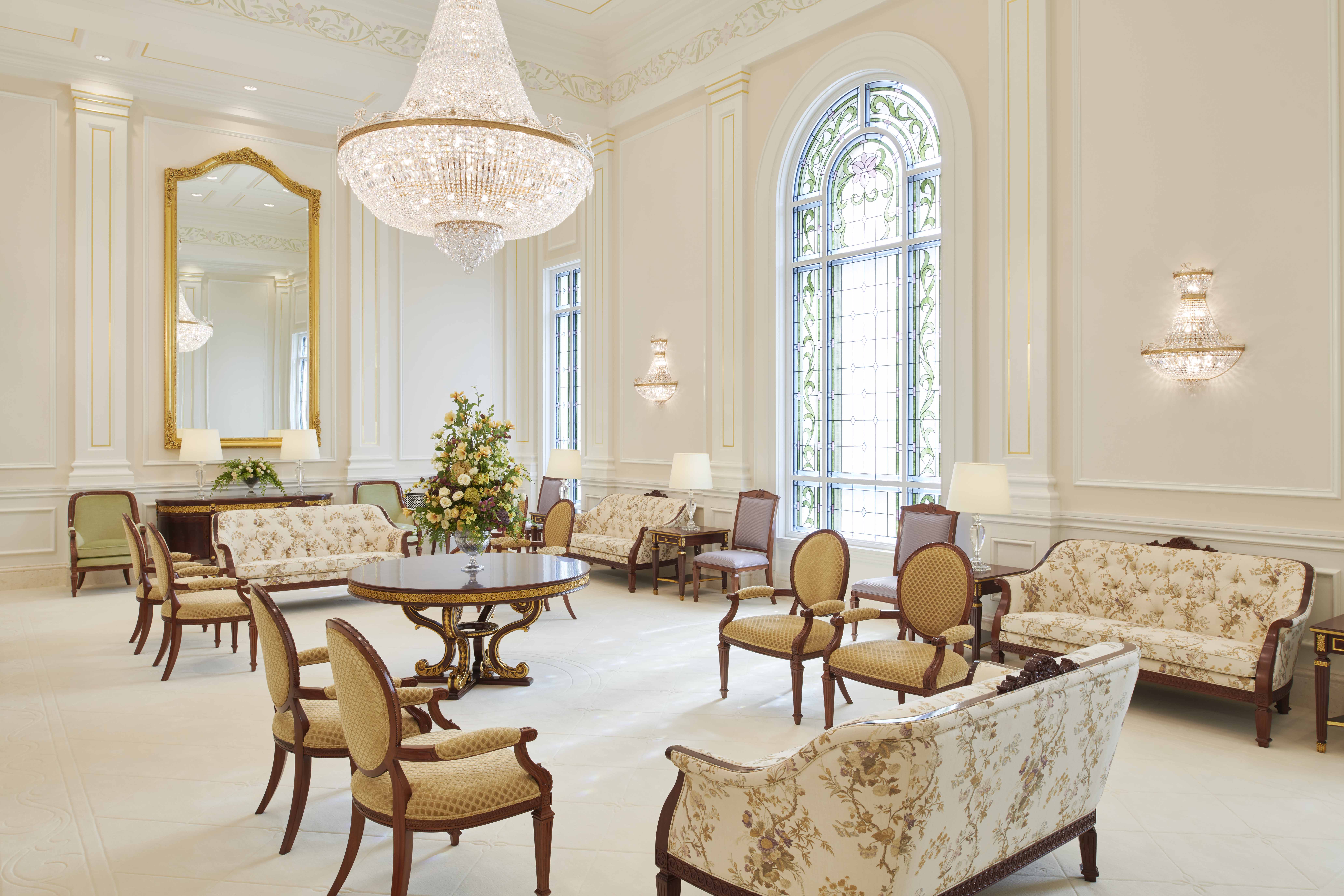 A white room contains a large chandelier and several couches and chairs.