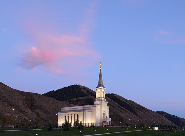 The Star Valley temple, a white building with a pale blue spire, stands in front of mountains at sunset.