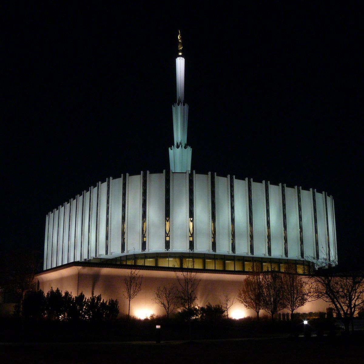 The exterior of the original Ogden Utah Temple, dedicated in 1972, that had a flat, round base with a spire in the center, at night.