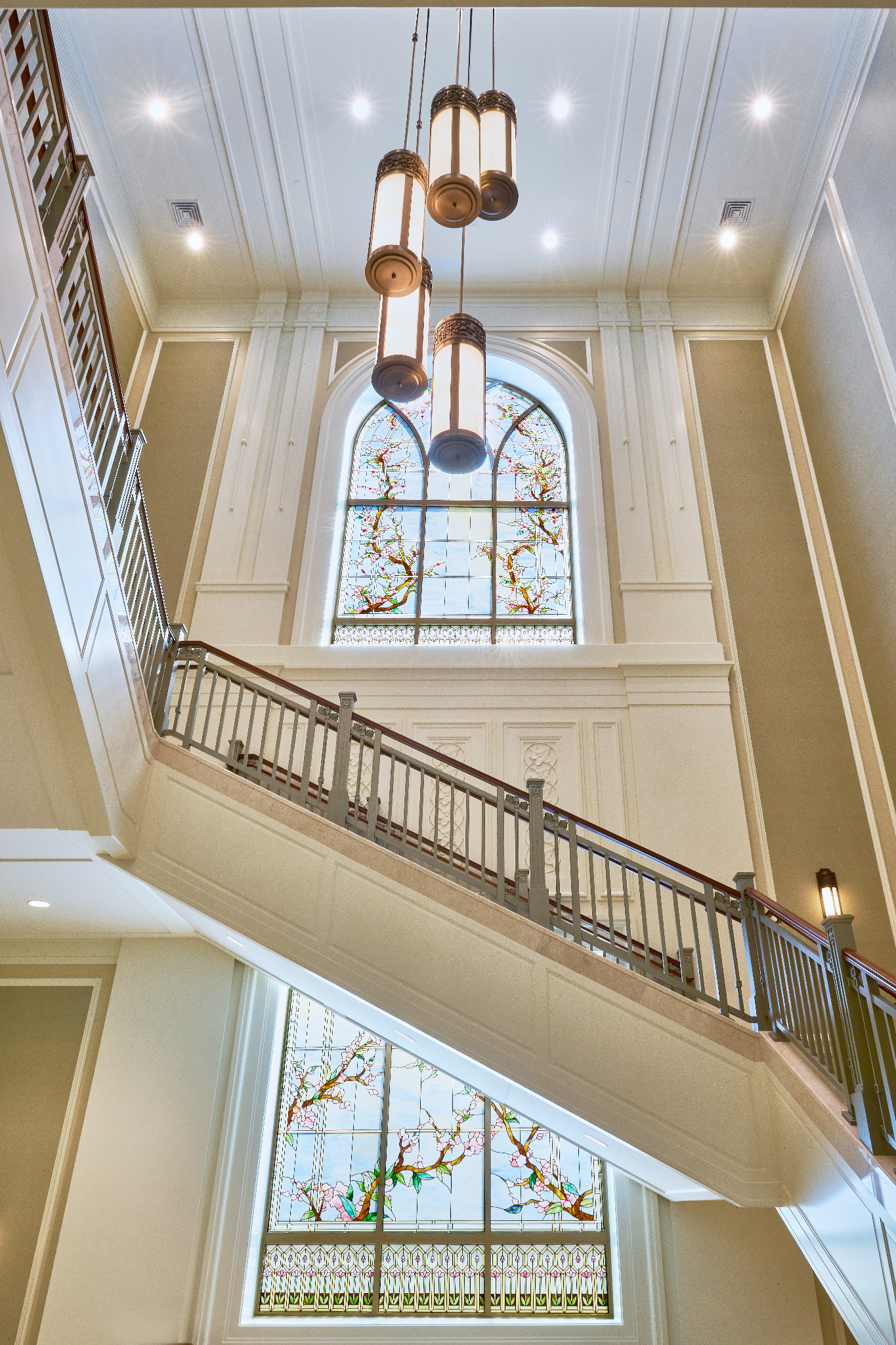 A low angle showing a tall staircase, with an arched, stained-glass window on the wall.