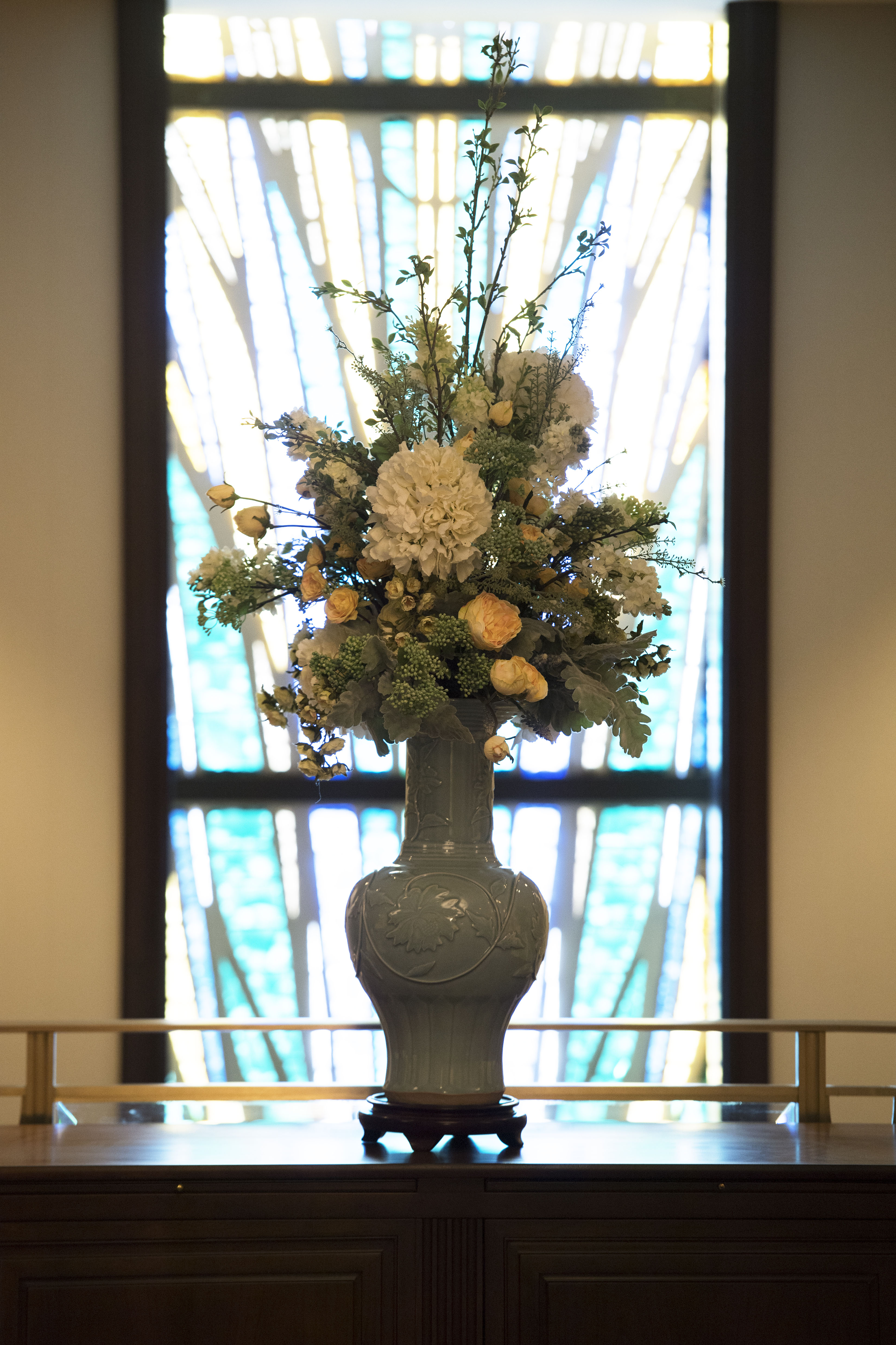 A close-up of flowers in a vase, with an art glass window behind it.