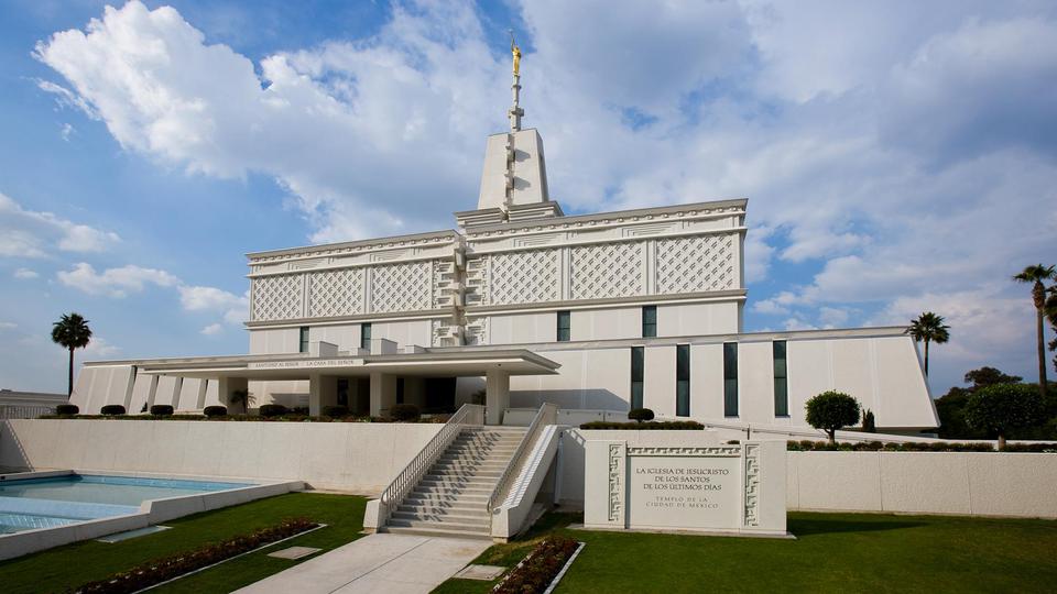 The exterior of the Mexico City temple, a white building with a basket-weave design and a spire with the angel Moroni on top.