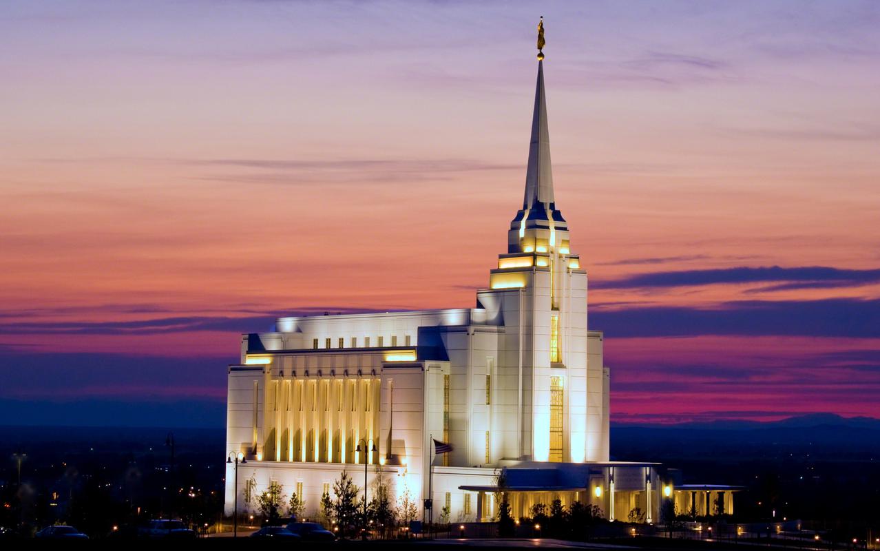 A dusk view of the illuminated Rexburg Idaho Temple, a white, rectangular building, with a sunset behind it.