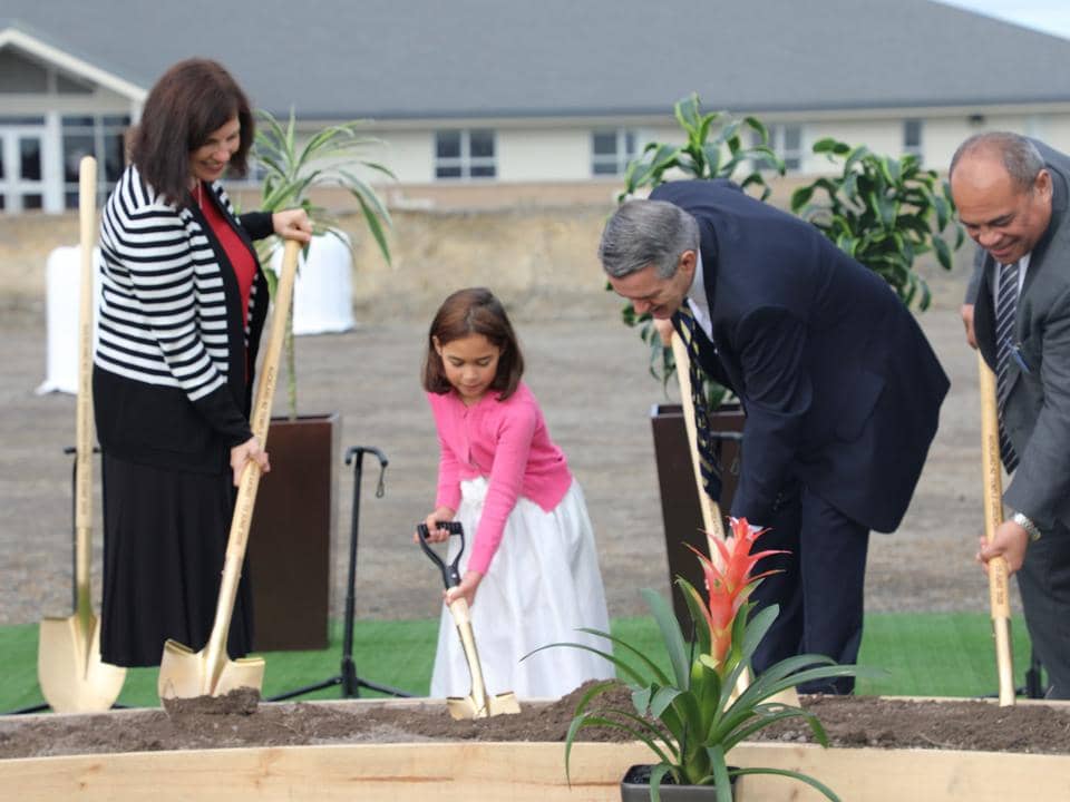 Two men, one woman and one Primary-aged girl in Sunday best holding ceremonial golden shovels in the ground and digging.