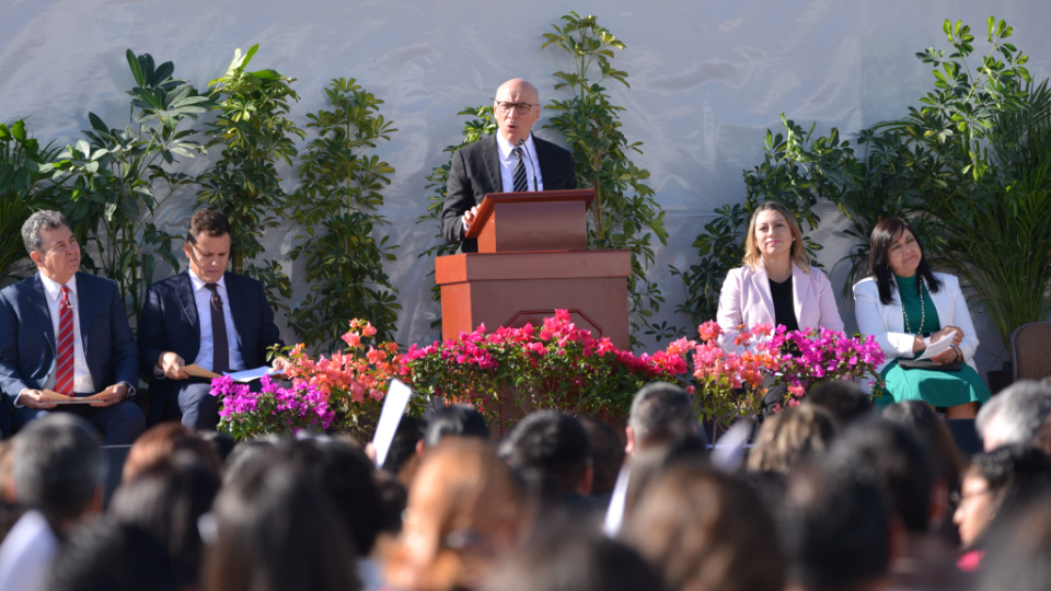 Elder Arnulfo Valenzuela of the Seventy speaking from a pulpit outside with a crowd of people listening to him.