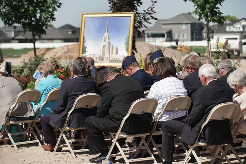 A congregation of people sitting in chairs outside and bowing their heads in prayer.