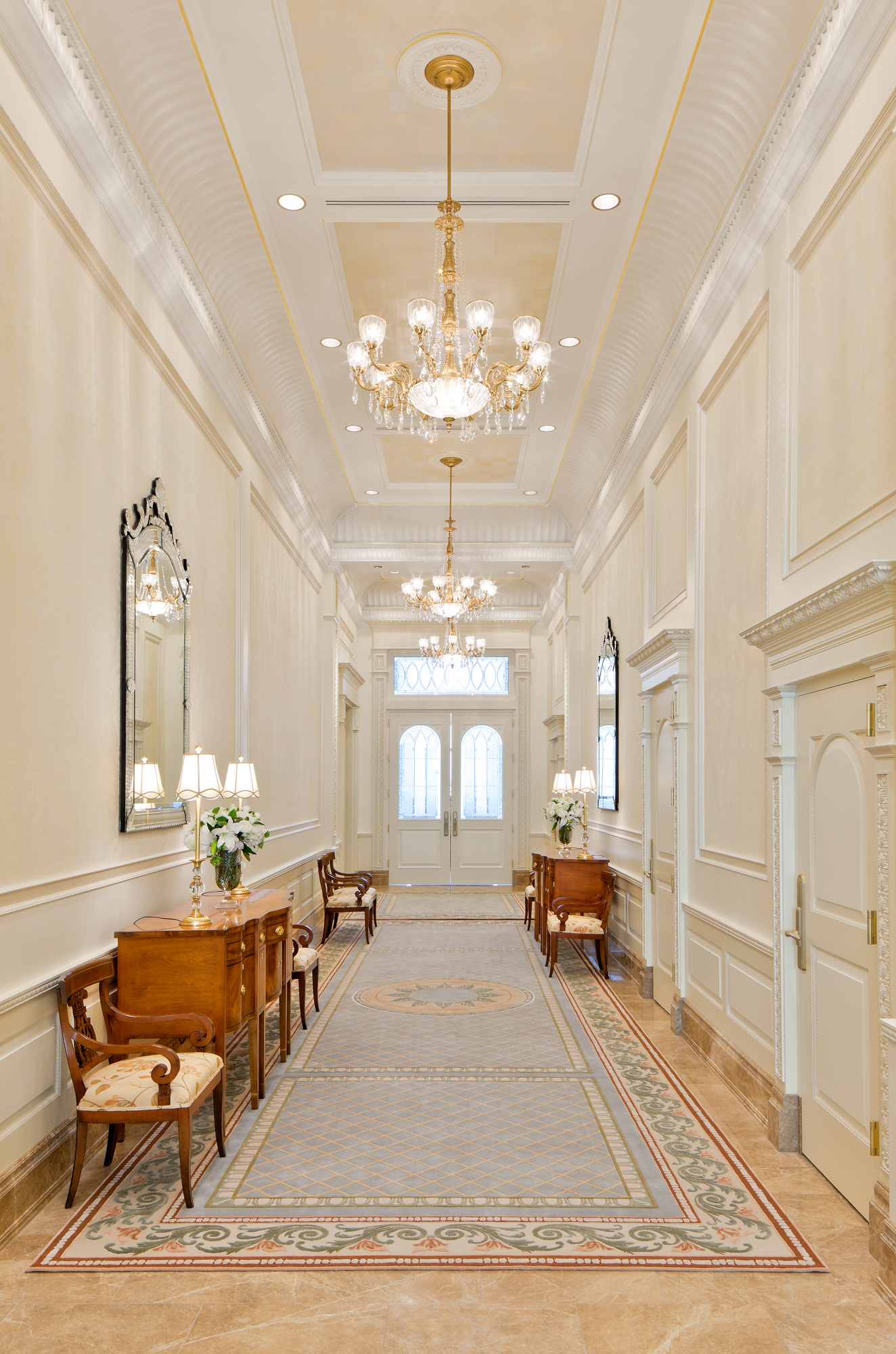 A white hallway with a large chandelier hanging from the ceiling.